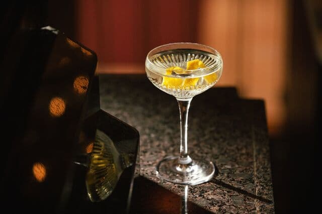 ATLAS martini service: etched coupe, citrus twist, lit from above.